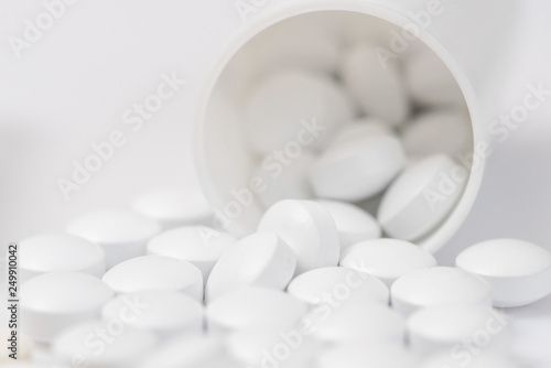 White pills spilling out of toppled pill bottle