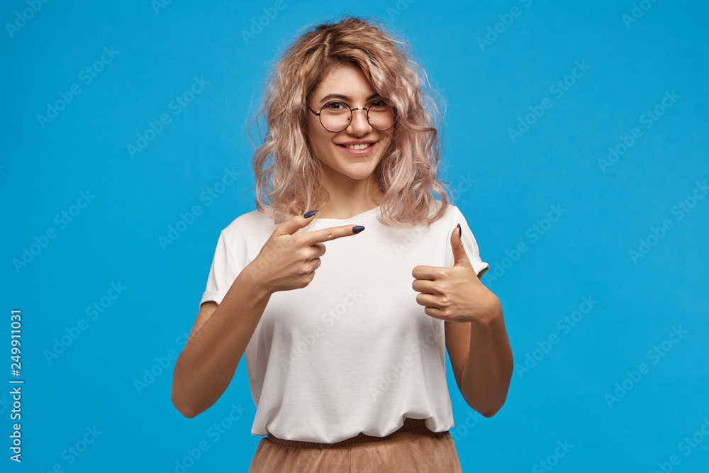 Check this out. Horizontal image of gorgeous charismatic young Caucasian woman with pinkish hair and long black nails showing thumbs up and pointing fore finger, smiling broadly, indicating copyspace Check this out. Horizontal image of gorgeous charismatic young Caucasian woman with pinkish hair and long black nails showing thumbs up and pointing fore finger, smiling broadly, indicating copyspace