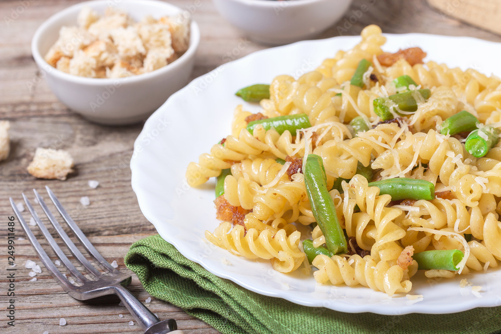 Traditional Italian Sicilian fusilli pasta with bread crumbs and green beans, sprinkled with cheese in a white plate on a wooden background. Tasty food