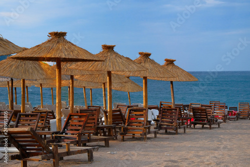 Beach chairs and straw umbrellas on tropical resort. Line of lounge chairs. Blue sea and sky on background. Summer vacations concept.