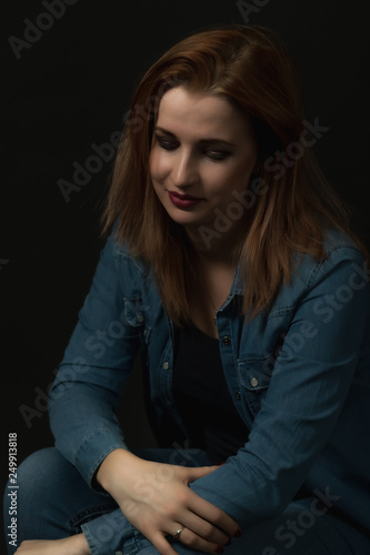 Low key portrait of young pensive woman sitting on the black background. Vertically.