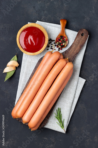 Canvas Print Raw frankfurter sausages with ketchup on cutting board. Top view.