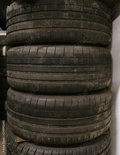 a tire stack with 3 used summer tires, placed over each other, the tire profile visible, in a workshop
