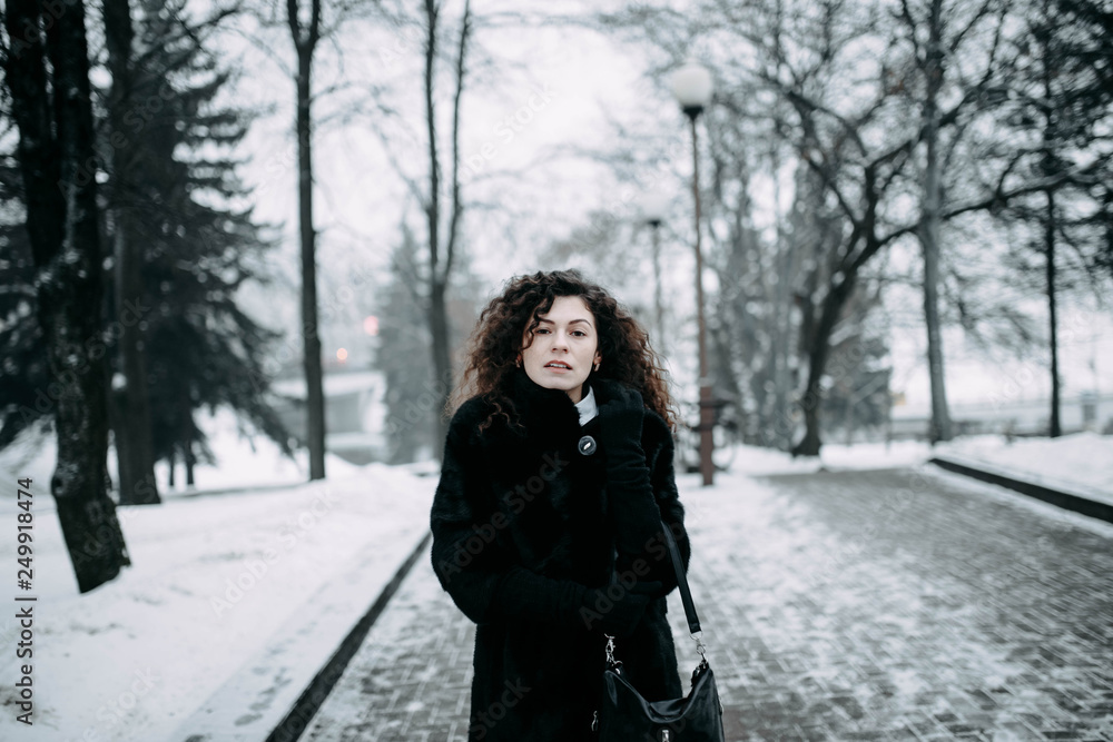 lonely curly brunette walks through a winter city in a fur coat lonely curly brunette walks through a winter city in a fur coat