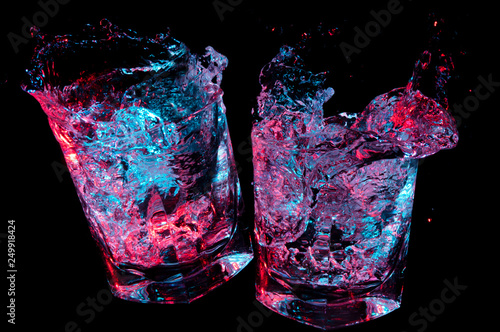 Two rocks glasses clinking in toast while glowing colorful liquid splashes out on a black background photo