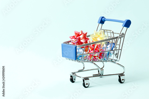 Buying gifts concept. Shopping cart full of gift bows and gifts on a blue background with space for text © PANDA
