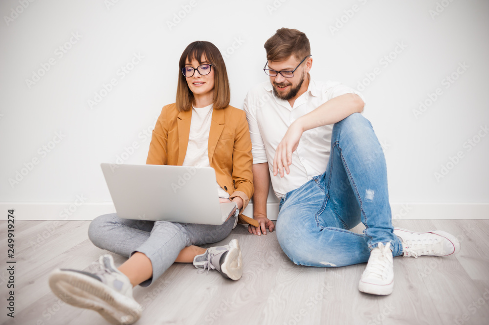 Two young coworkers dressed casual using laptop in white interior Two young coworkers dressed casual using laptop in white interior