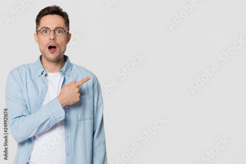 Shocked stunned young man nerd pointing finger aside at copyspace