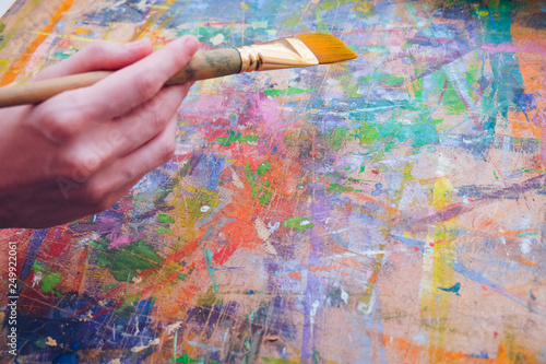 Female artist's hand hold paintbrush and painting a colorful abstract picture with many splatters.