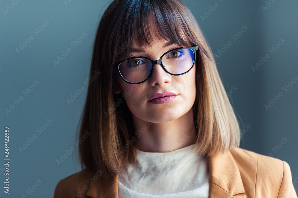 Fototapeta premium Smiling brunette woman in eyeglasses posing with crossed arms and looking at the camera over grey background