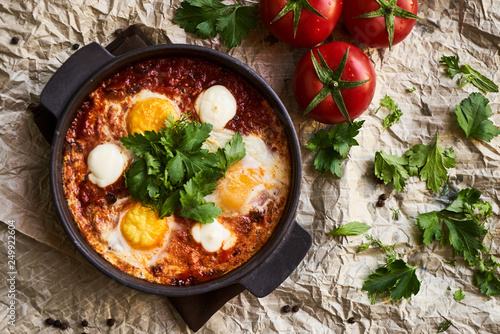 Shakshuka with eggs, tomatoes and parsley in a frying pan, close-up