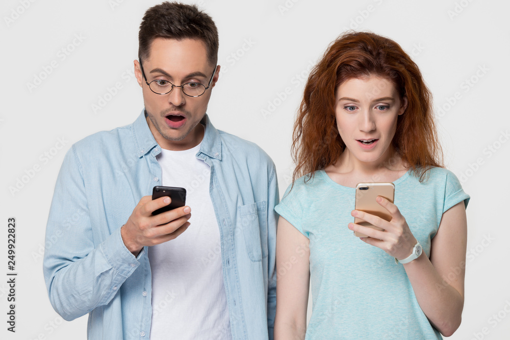 Surprised couple holding phones amazed by mobile app sms offer