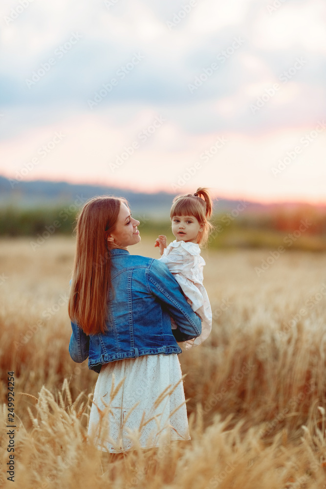 girl in white dress in the arms of mothers in a field of wheat