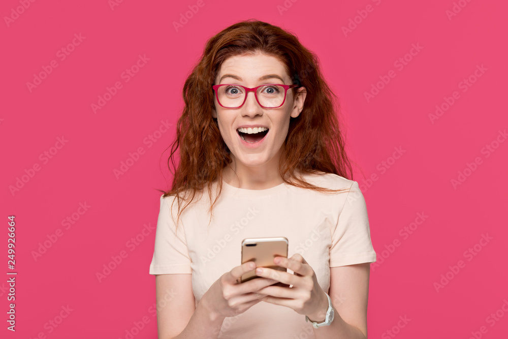 Excited redhead woman holding cell phone amazed by mobile win Excited redhead woman holding cell phone amazed by mobile win