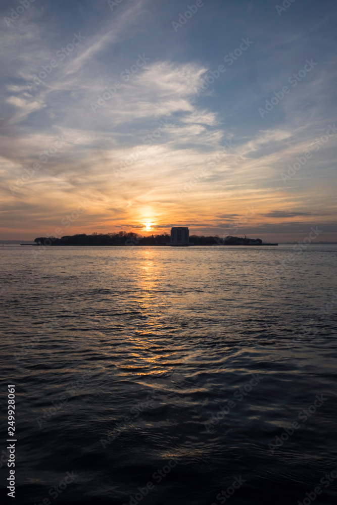 Fototapeta premium sunset over island in harbor with clouds and waves