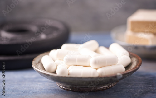 Creatine capsules, Protein bar in two pieces and plates. Nutrition for bodybuilding. Fitness supplements on rustic wooden background. Close up. 