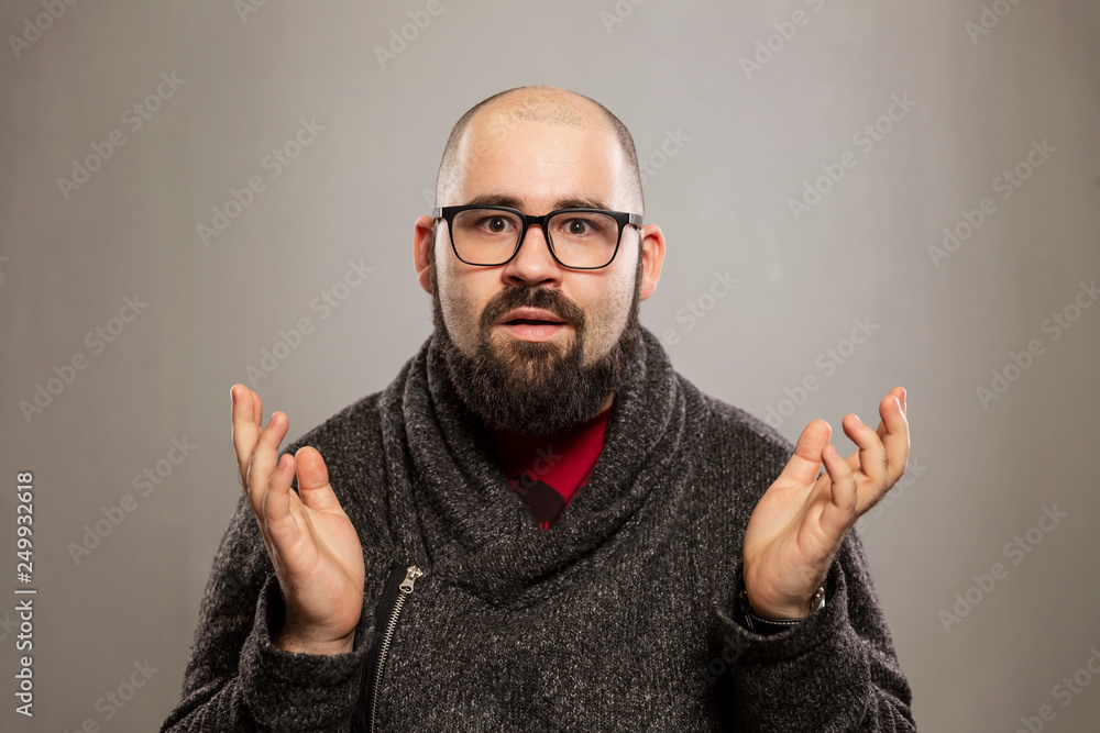 Young bald man spreads his arms in confusion, gray background Young bald man spreads his arms in confusion, gray background