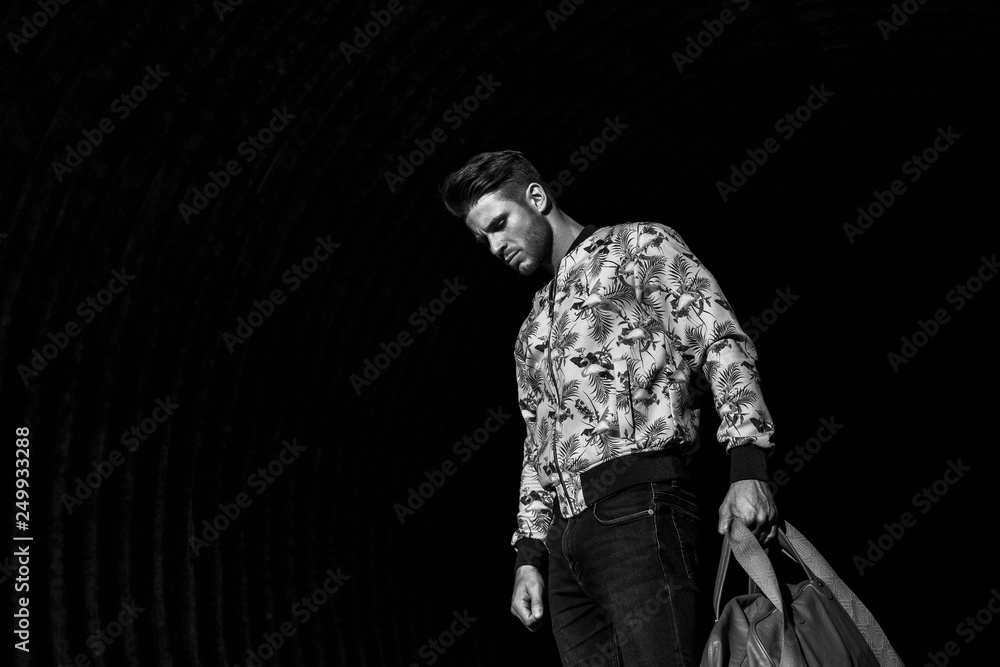 Sexy muscular young model with beard on dark background. Fashion portrait of brutal strong guy in trendy clothes and hairstyle. Fashion concept. Black and white. Stylish man traveling with a bag. Sexy muscular young model with beard on dark background. Fashion portrait of brutal strong guy in trendy clothes and hairstyle. Fashion concept. Black and white. Stylish man traveling with a bag.