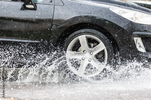 Car motion through big puddle of water splashes from the wheels on the street road. Water splash rain texture