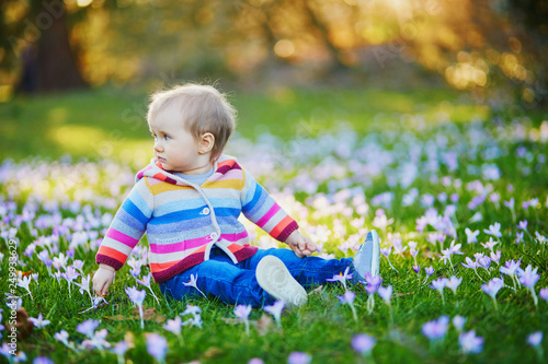 Baby girl in knitted clothes sitting on the grass with blue hyacinths