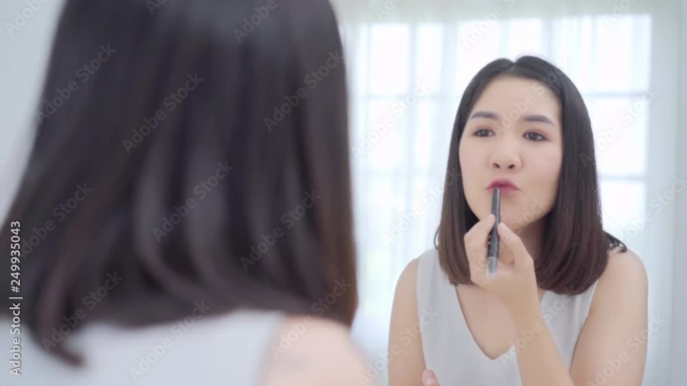 Beautiful Asian woman using lipstick make up in front mirror, Happy female using beauty cosmetics to improve herself ready to working in bedroom at home. Lifestyle women relax at home concept. Beautiful Asian woman using lipstick make up in front mirror, Happy female using beauty cosmetics to improve herself ready to working in bedroom at home. Lifestyle women relax at home concept.