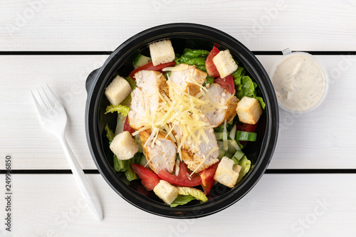 Caesar salad in round black lunchbox on wooden bacground