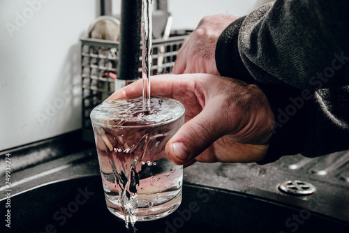 Pouring water into a glass. Man pours water from a black tap into a transparent glass. The concept of saving water, problems with water, lack of water in various regions of the world.