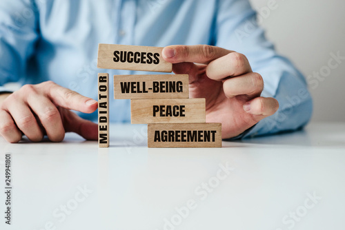 The role of the mediator in maintaining stability in life. Man arranges wooden blocks with inscription PEACE, AGREEMENT supported by a wooden MEDIATOR block. Role of mediation in maintaining order.
