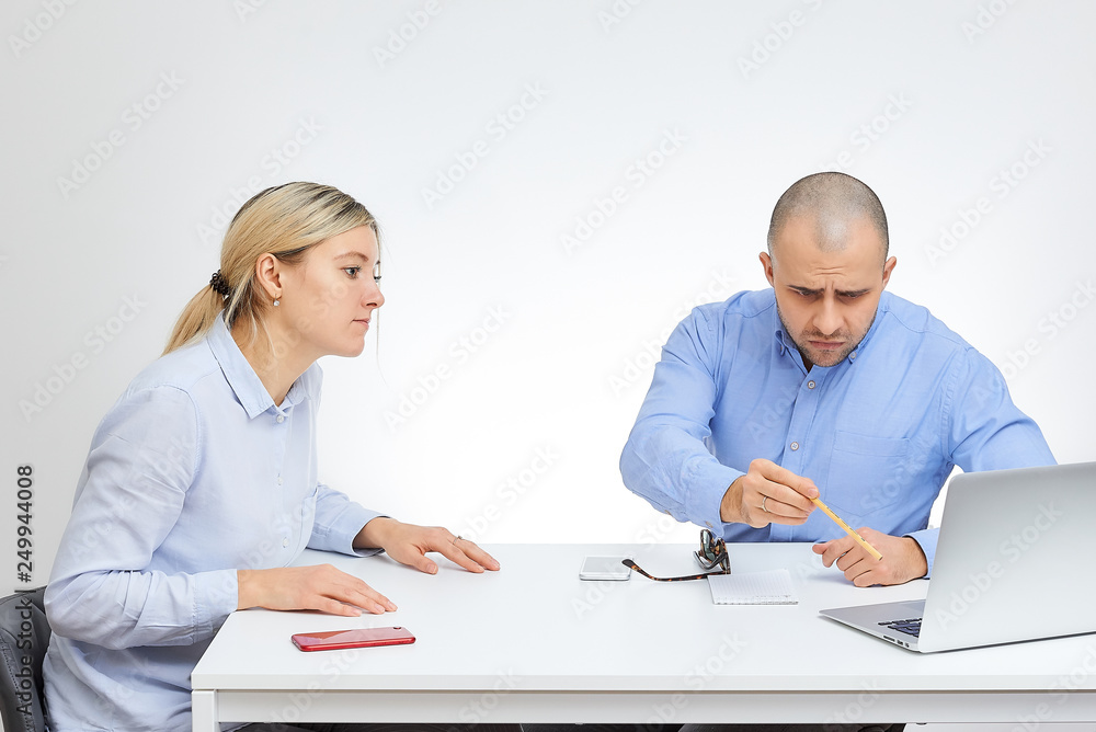 Brutal boss in a blue shirt in stylish sunglasses takes a selfie near his blonde caucasian colleague sits by the desk in the office with the white background. Brutal boss in a blue shirt in stylish sunglasses takes a selfie near his blonde caucasian colleague sits by the desk in the office with the white background.