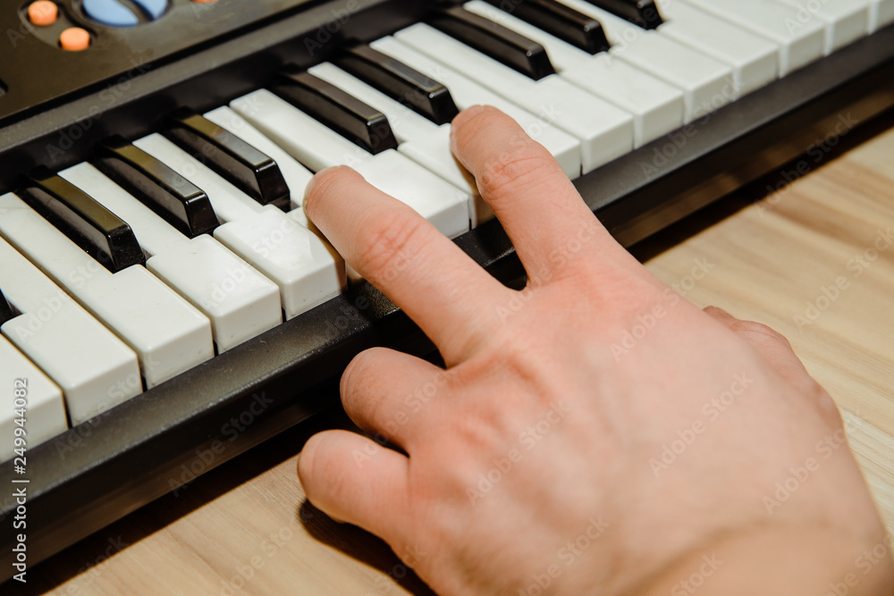 Fototapeta premium The man is pressing his finger on the electric organ key. The concept of playing the piano, piano. Learning music.