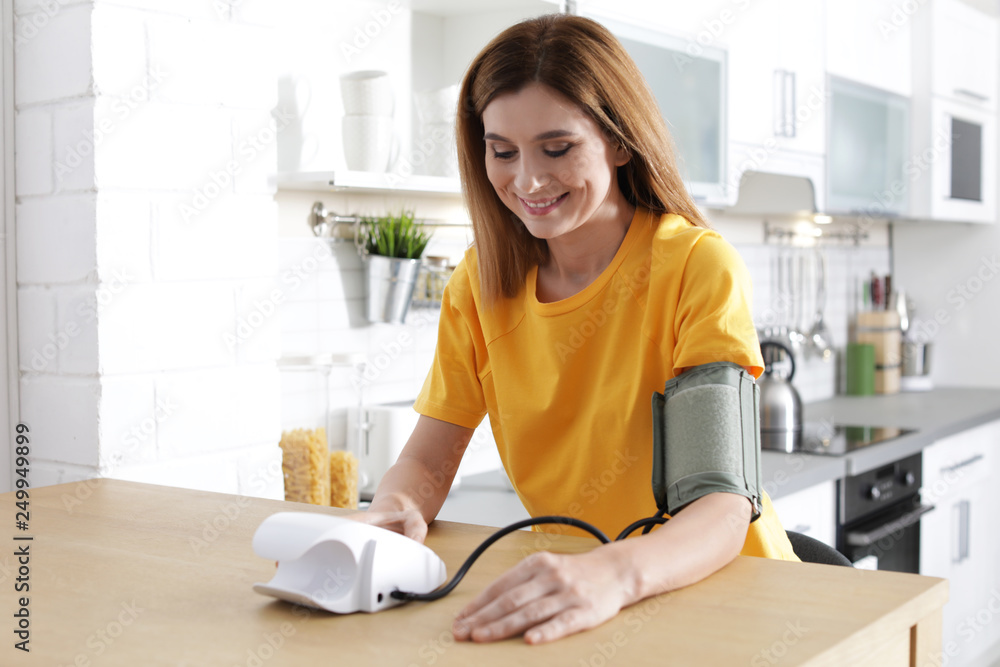 Woman checking blood pressure with sphygmomanometer at table indoors. Cardiology concept Woman checking blood pressure with sphygmomanometer at table indoors. Cardiology concept