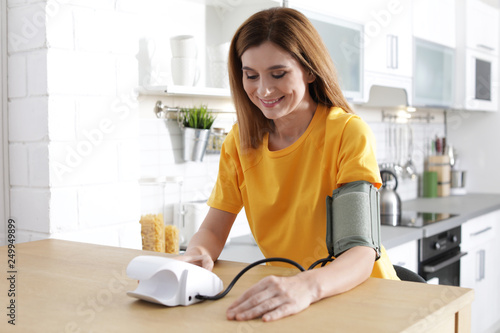 Foto Woman checking blood pressure with sphygmomanometer at table indoors