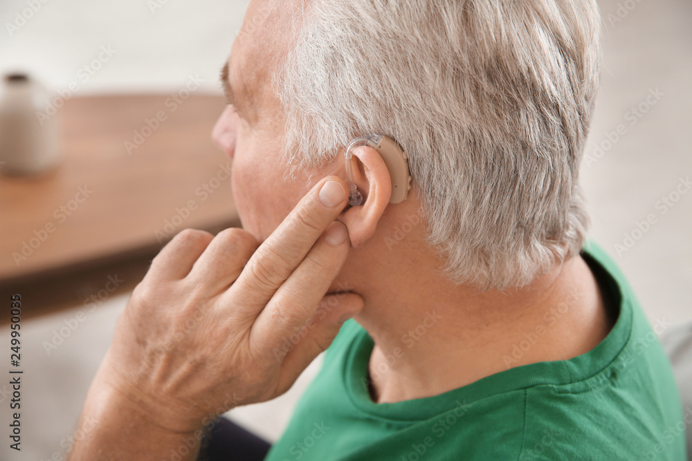 Mature man adjusting hearing aid at home, closeup Mature man adjusting hearing aid at home, closeup