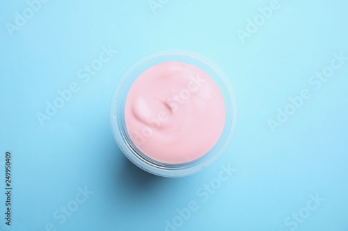 Plastic cup with creamy yogurt on color background, top view