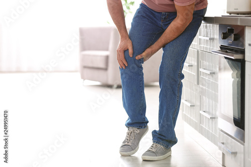 Senior man suffering from knee pain in kitchen, closeup. Space for text