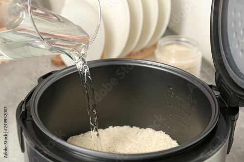 Water pouring into modern rice cooker in kitchen