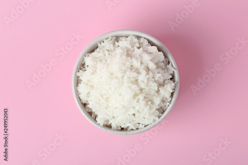 Bowl of boiled rice on color background, top view