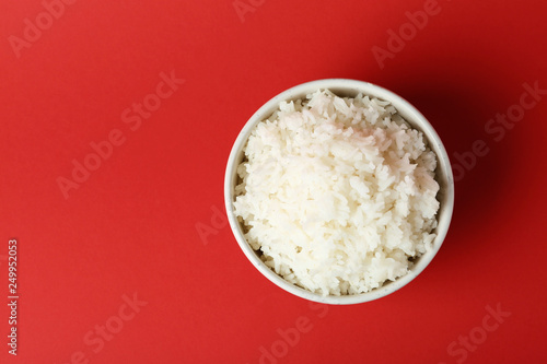 Bowl of boiled rice on color background, top view with space for text
