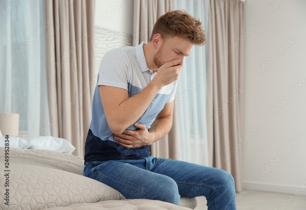 Young man having nausea in bedroom. Feeling sick Young man having nausea in bedroom. Feeling sick