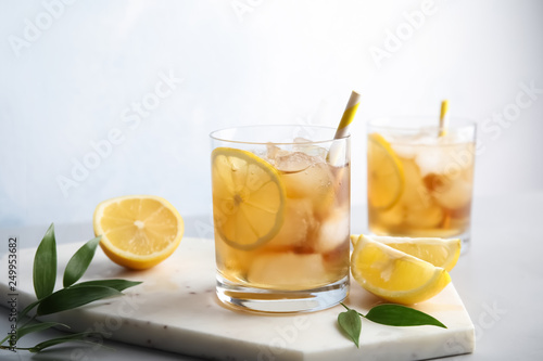 Glasses of lemonade with ice cubes on table against light background. Space for text