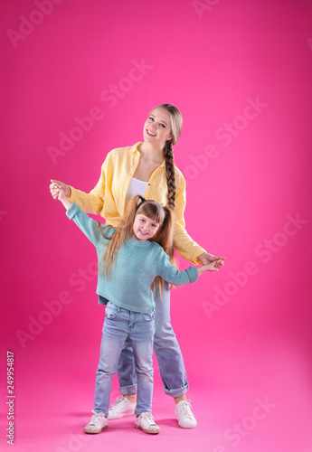 Happy woman and daughter in stylish clothes on color background