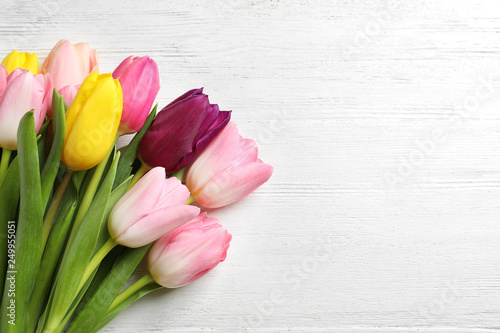 Beautiful spring tulips on light wooden background, top view with space for text. International Women's Day