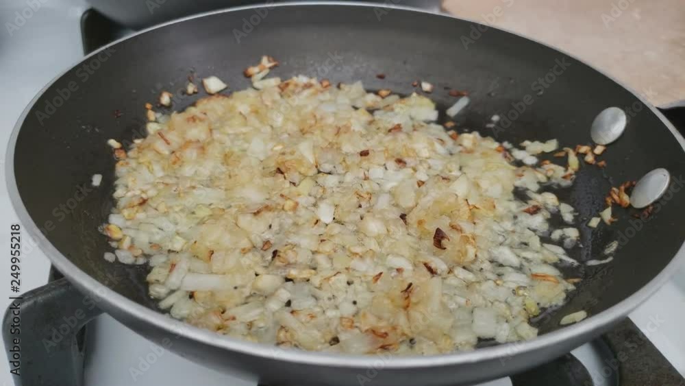 Home cooking - Close up of shaking or mixing minced onion being saute or quick fry in hot oil in small non-stick pan over gas stove. Home cooking - Close up of shaking or mixing minced onion being saute or quick fry in hot oil in small non-stick pan over gas stove.