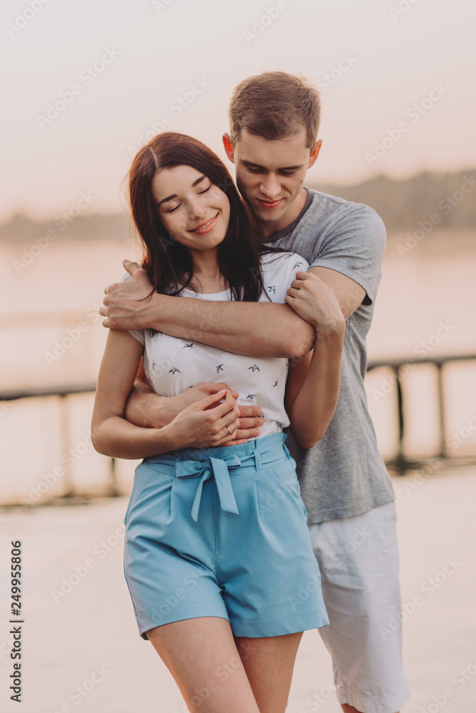 Loving young couple hugging on pier at sunset in summer. Loving young couple hugging on pier at sunset in summer.