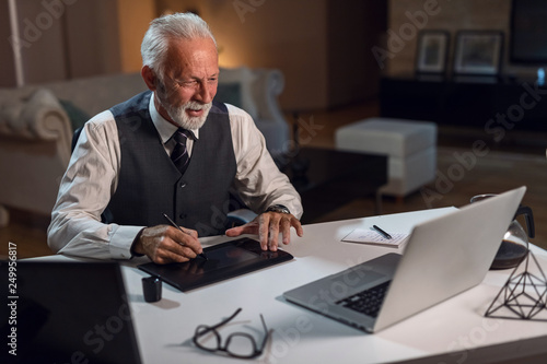 Happy mature editor using digitized pen while working on computer in his office. photo