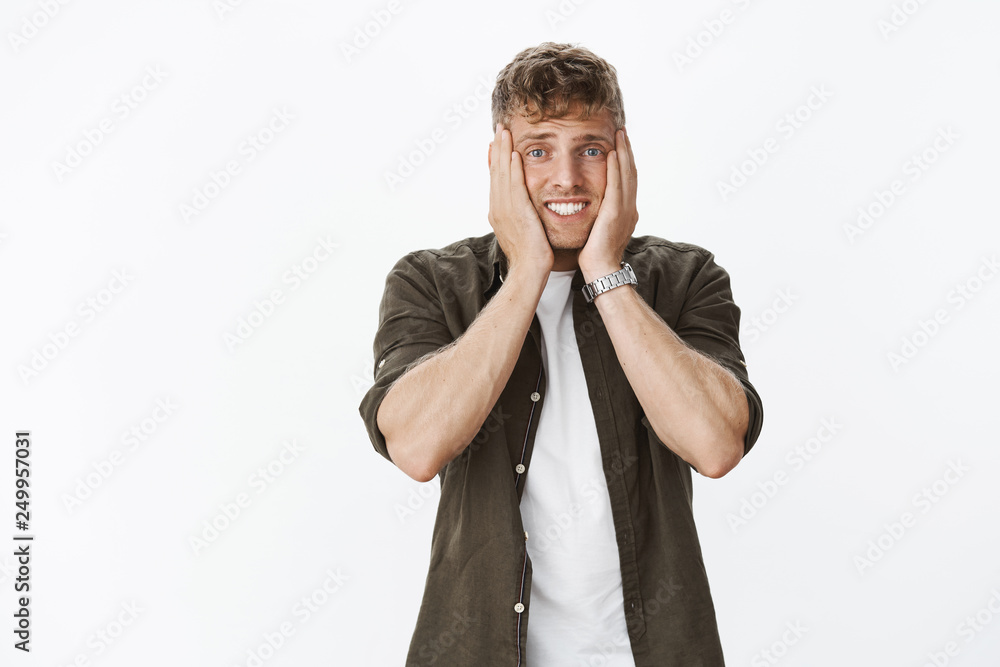 Anxious and shocked troubled cute mature blond european male with bristle squeezing face in palms and clenching teeth looking scared at camera as having problem, worry over gray background Anxious and shocked troubled cute mature blond european male with bristle squeezing face in palms and clenching teeth looking scared at camera as having problem, worry over gray background