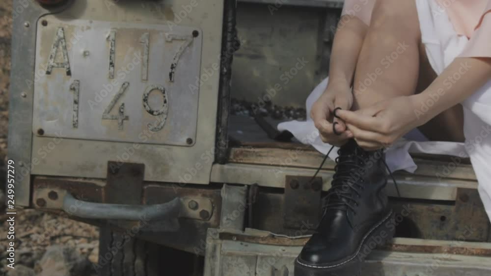 Dolly in shot of sexy blonde woman in white skirt and black shoes tying shoelaces sitting in abandoned pickup truck. Dolly in shot of sexy blonde woman in white skirt and black shoes tying shoelaces sitting in abandoned pickup truck.
