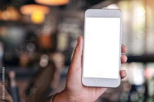 Mockup image of hand holding and showing a white mobile phone with blank screen with blurred background in cafe