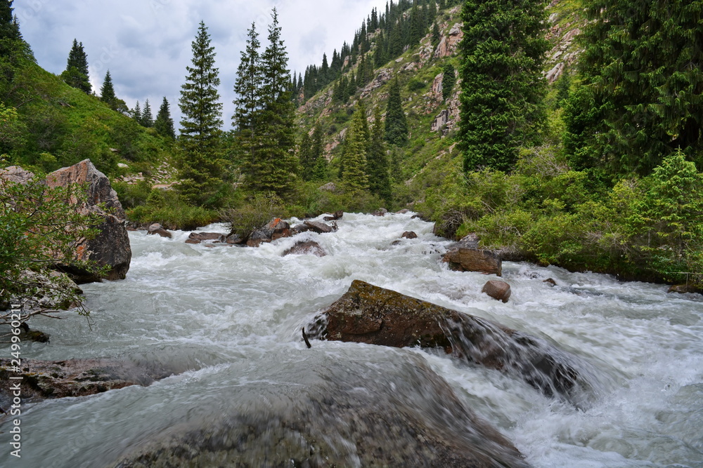 Speed turbulent water stream with white foam in the mountain river between rocks and boulders after hard rain. Shot at long exposure, blurred water Speed turbulent water stream with white foam in the mountain river between rocks and boulders after hard rain. Shot at long exposure, blurred water