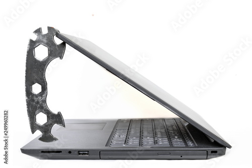 Concept of computer repair and maintenance. Metal multifunctional wrench holds notebook open cover of lcd display on white background. Isolated, side view photo